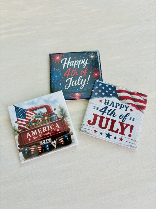 Three magnets with 4th of July designs on a light wooden surface.