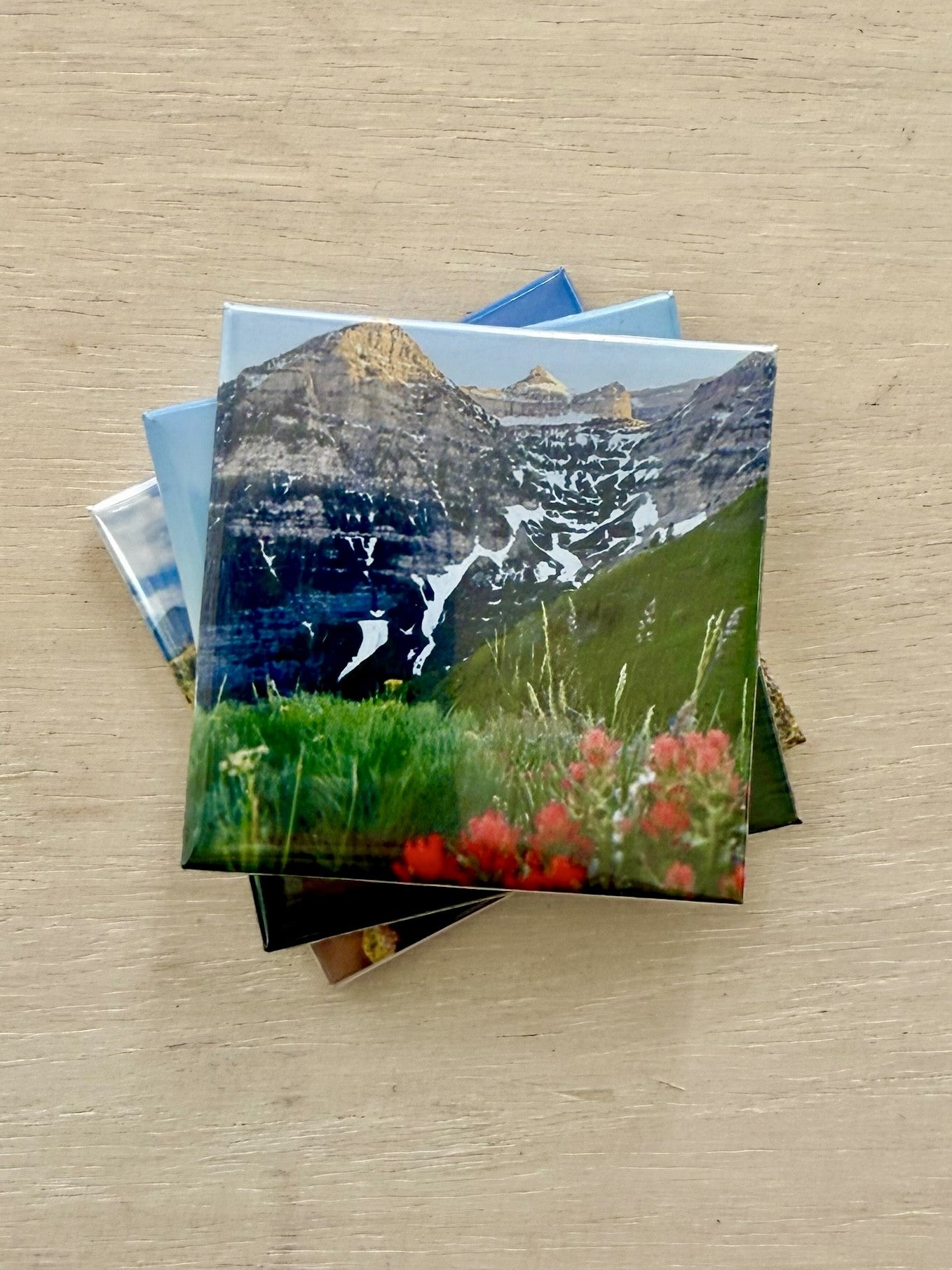Small stack of photo magnets with mountain and nature scenes on a wooden surface.