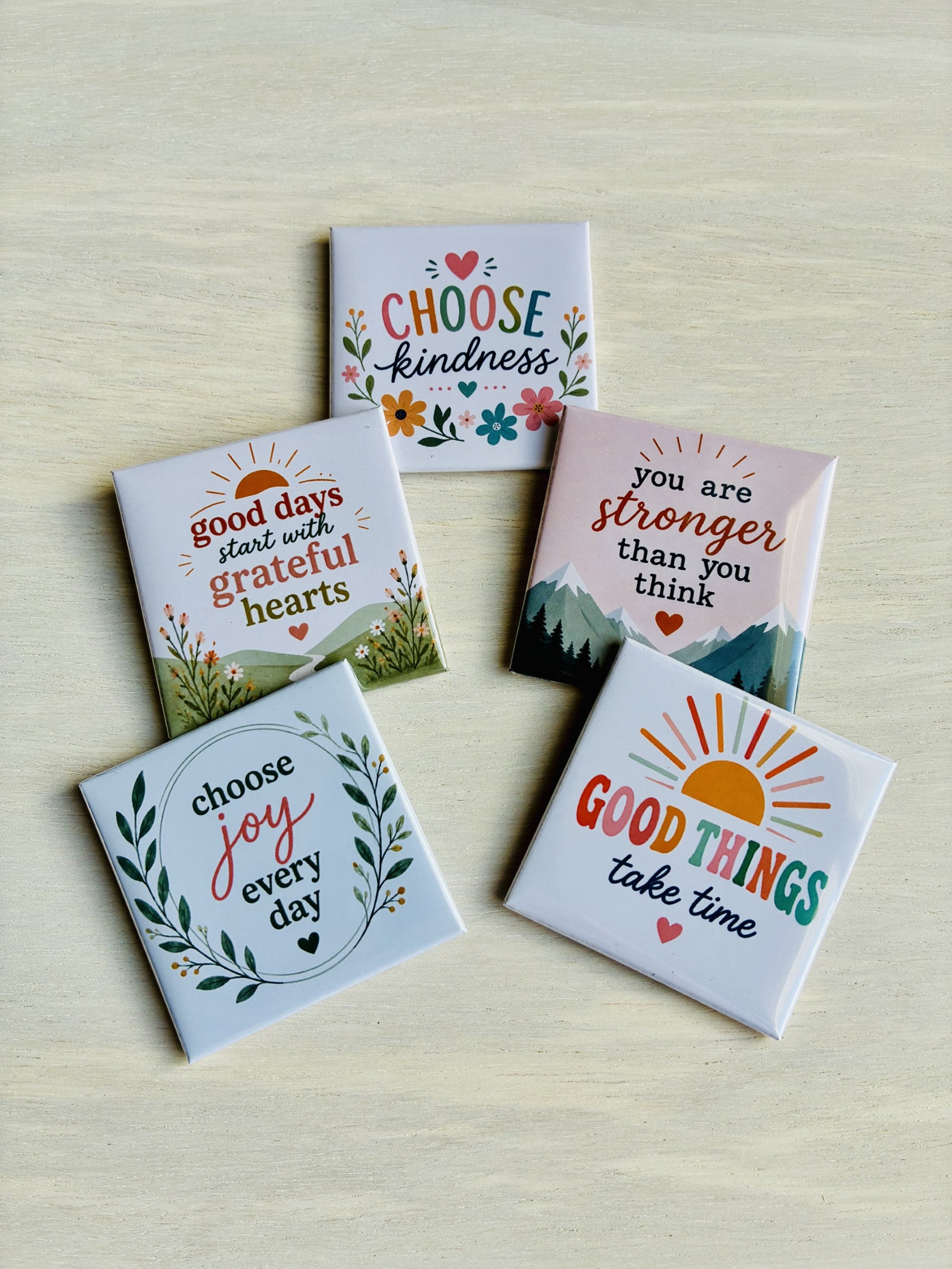 Set of five motivational magnets with inspirational phrases on a light wooden surface.